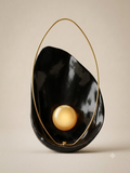An organically designed lighting unit inspired by seashells, featuring a glossy black background that embraces a pearl-like luminous sphere within a delicate gold frame.