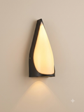 A wall lamp with a simple, streamlined design that mimics a water droplet or a flame, combining a dark metal frame and frosted glass that distributes warm and calming light.