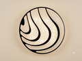 A circular lighting unit with a streamlined design that mimics sand dunes or waterways, combining hollow lines and luminous surfaces with a grainy texture to distribute warm and attractive lighting.
