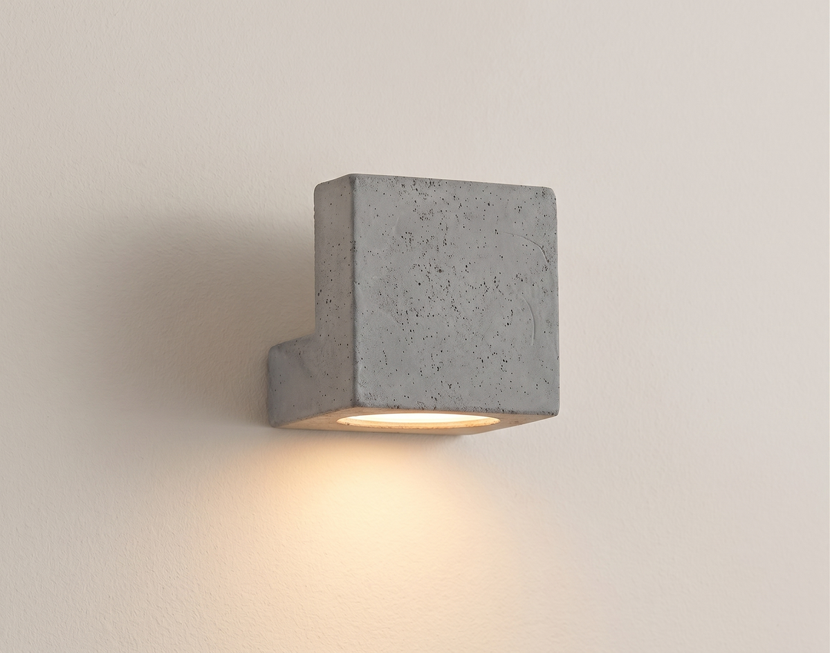 A wall lamp with a simple geometric design made of industrial-style concrete, reflecting a modern architectural aesthetic and providing warm under-lighting.