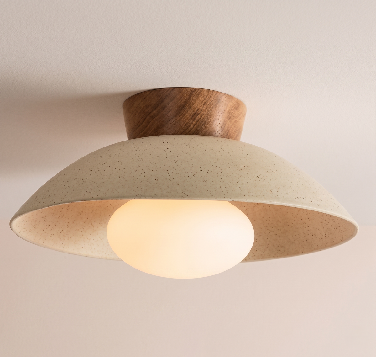 A ceiling light fixture with a nature-inspired design, combining the warmth of wood with a dotted stone texture, and featuring a radiant glass sphere in the center to distribute soft light.